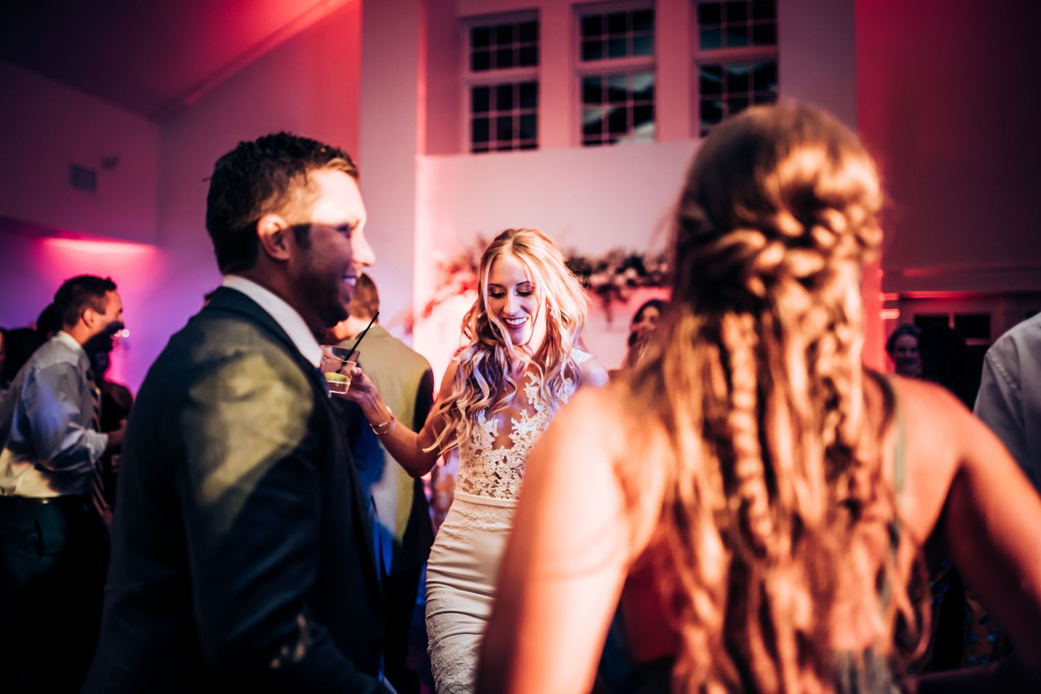 Dance floor moment captured under pink and purple lighting at a wedding reception.