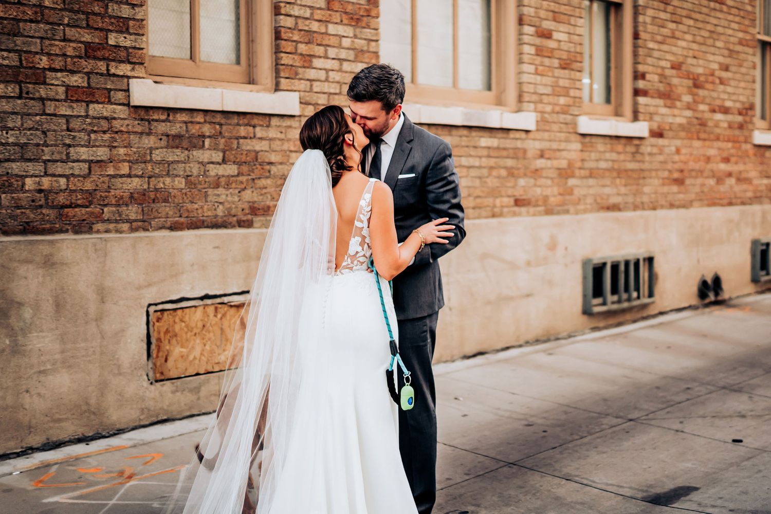 A tender wedding moment captured against a brick wall backdrop in an urban setting.
