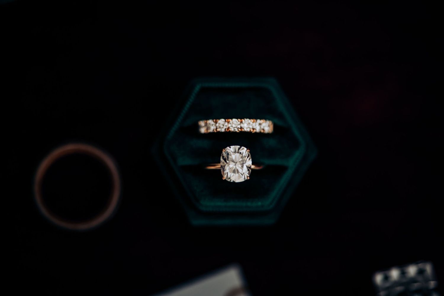 Diamond engagement ring in teal hexagonal box against dark background.