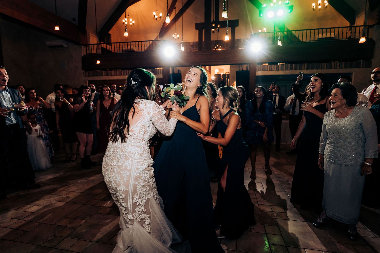 Wedding celebration with guests dancing under indoor lighting at evening reception.