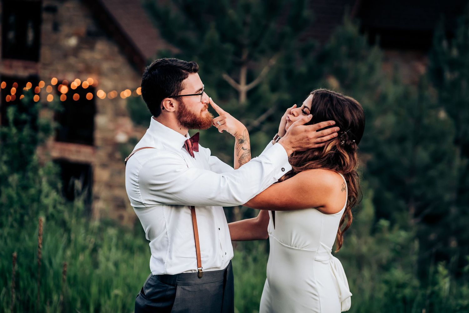 Intimate wedding moment captured at dusk with string lights and mountains in background.