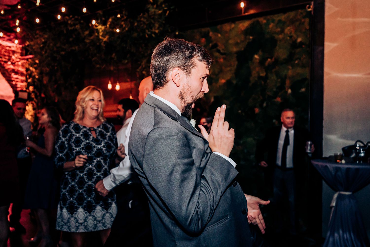 Guest celebrating enthusiastically during wedding reception with string lights in background.