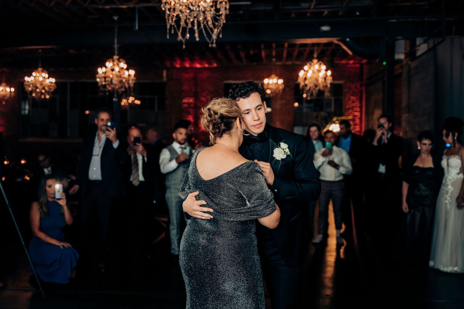Wedding dance under crystal chandeliers in an elegant venue with guests watching.
