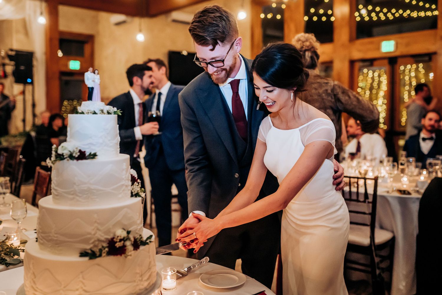 A couple cuts their elegant white wedding cake together during their reception celebration.