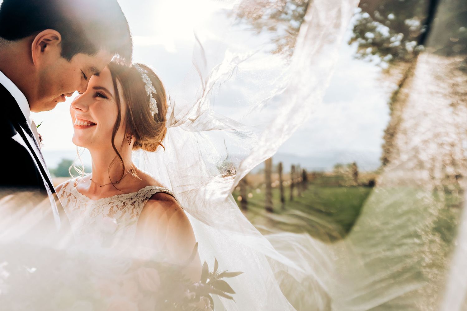 A romantic wedding photoshoot with sunlit veil and scenic countryside background in soft light.