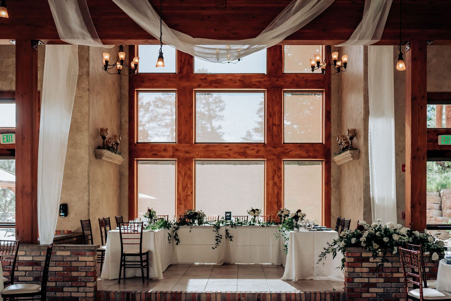 Rustic wedding venue interior with wooden beams, white draping, and floral decorations.