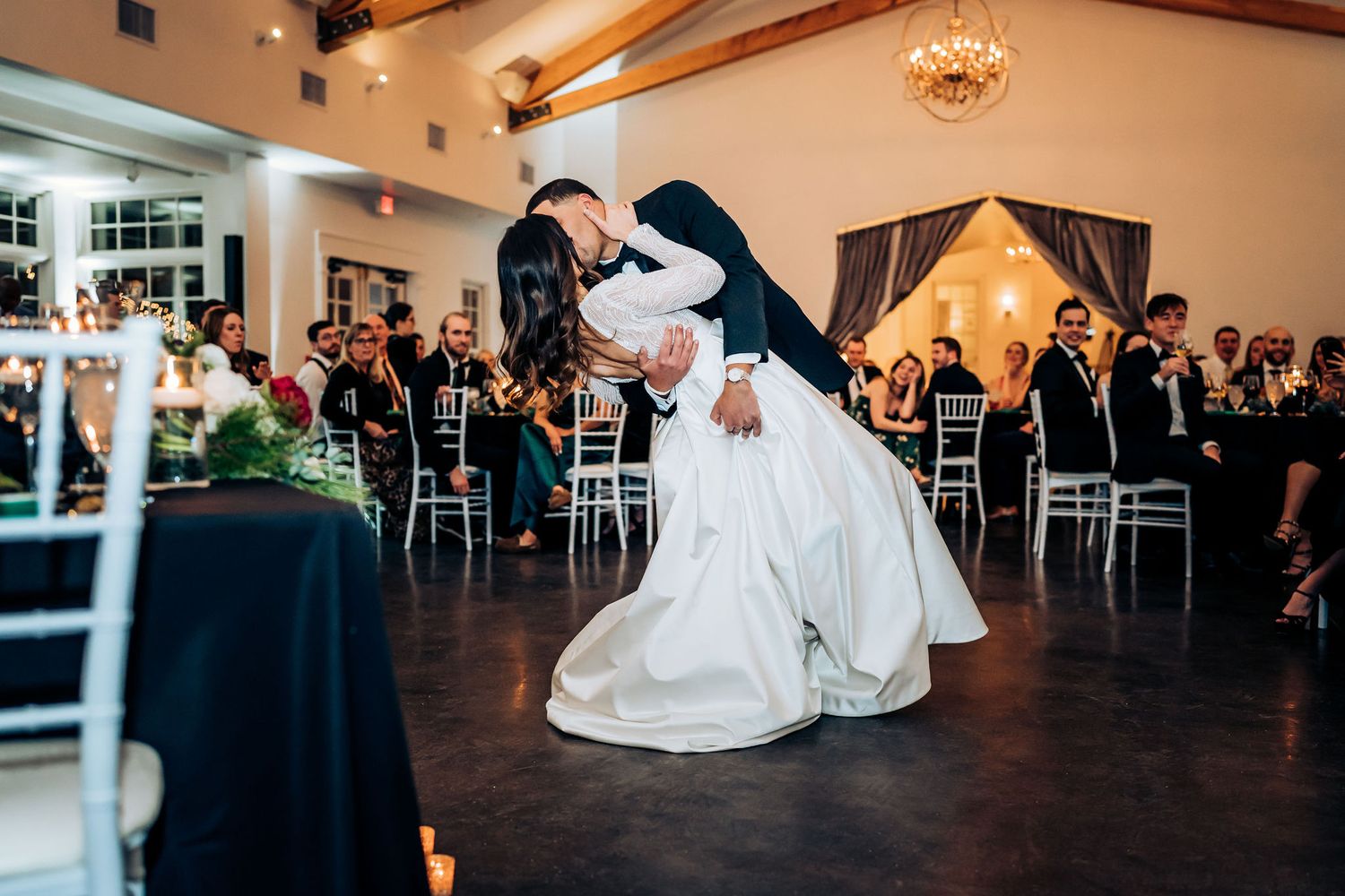 Couple performs dramatic dance dip during wedding reception in elegant venue with wooden beams.