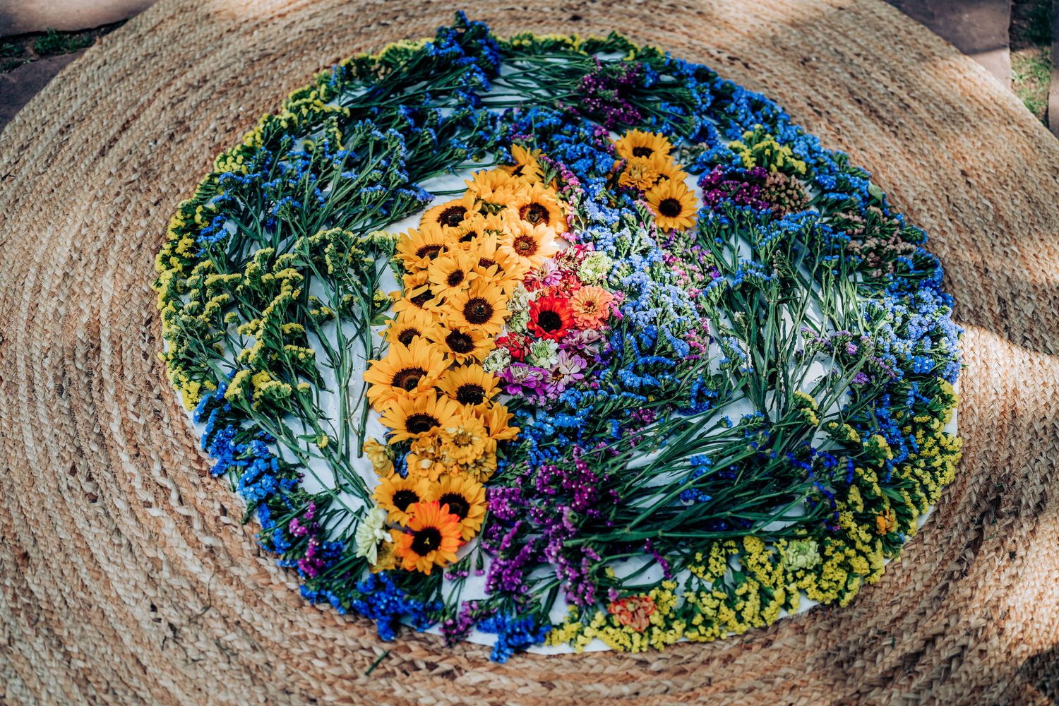 A colorful mandala made of sunflowers and blue flowers arranged on a wooden surface.