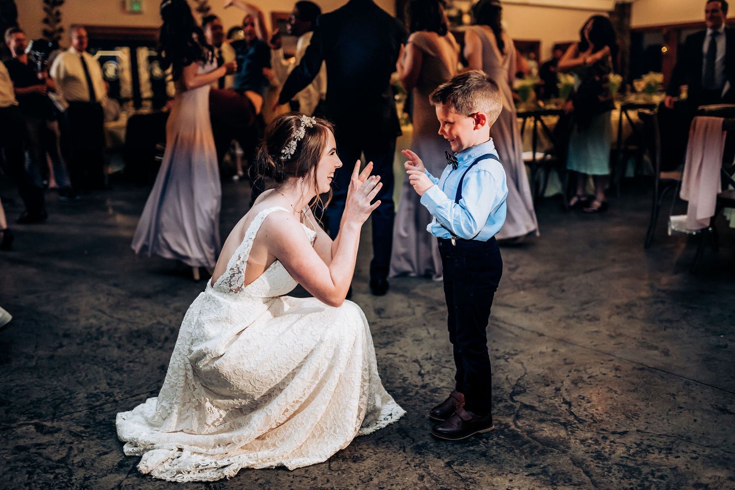 A sweet moment between a bride in a lace gown and a young ring bearer at a wedding reception.