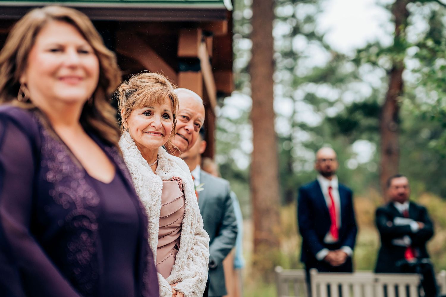 Wedding guests gather outdoors among pine trees during a mountain ceremony.