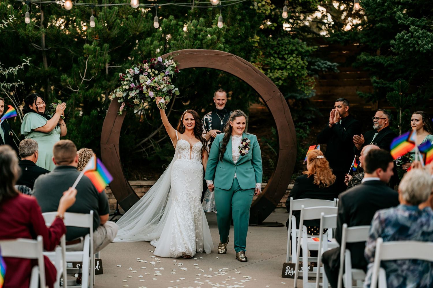 Outdoor wedding ceremony setup with white chairs and wooden arch surrounded by greenery.