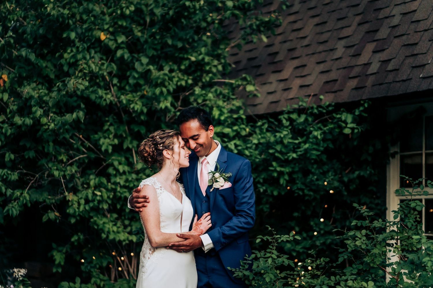 A couple embraces in front of lush green foliage during their wedding portraits.