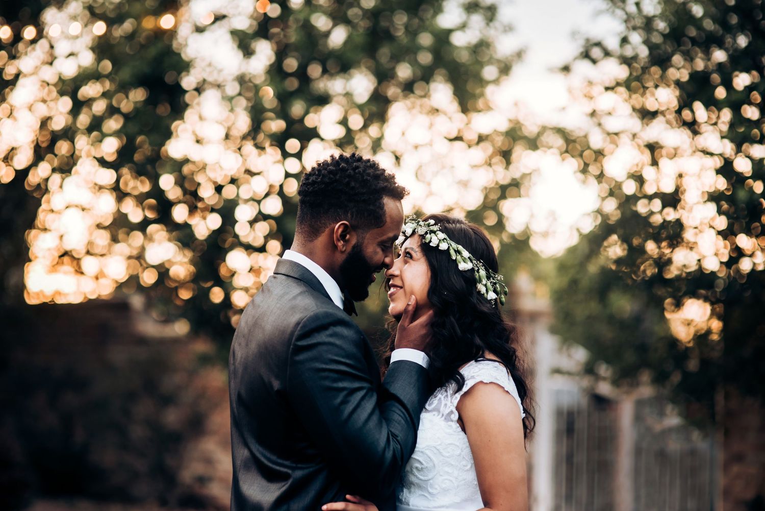 Romantic sunset wedding portrait with golden bokeh light effects through trees.