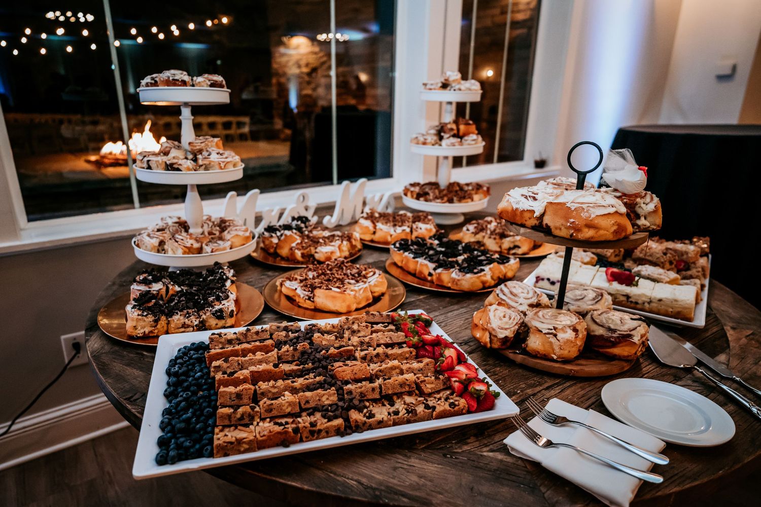 Elegant wedding dessert table with tiered cake stands, fruit pastries, and assorted sweets at a reception venue.