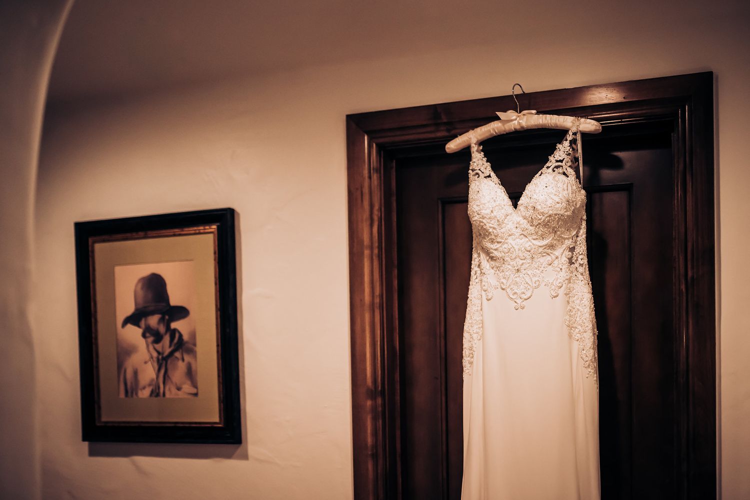 Elegant white wedding dress hanging in doorway with framed artwork on wall.