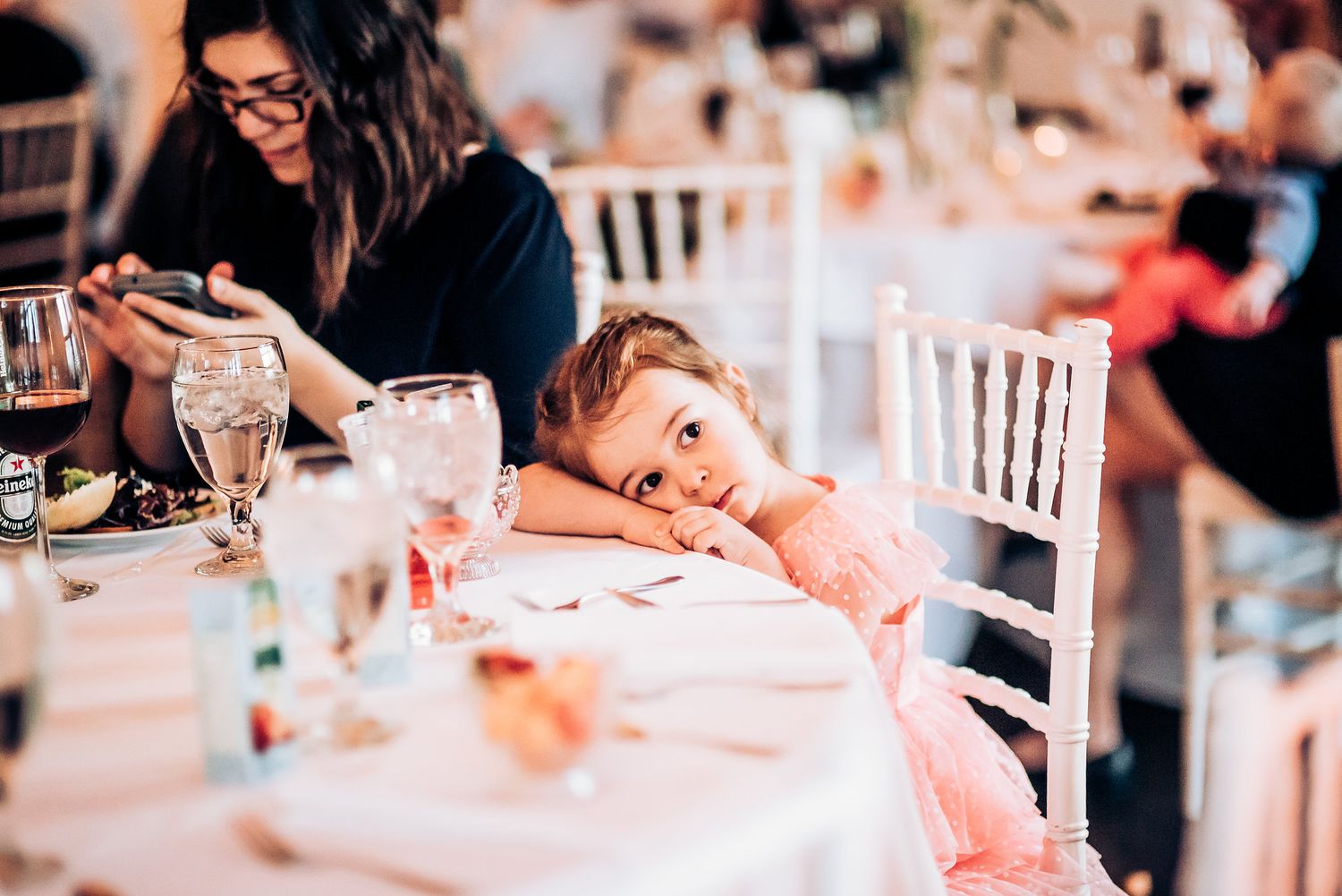 Young guest in pink dress rests head on table during wedding reception.