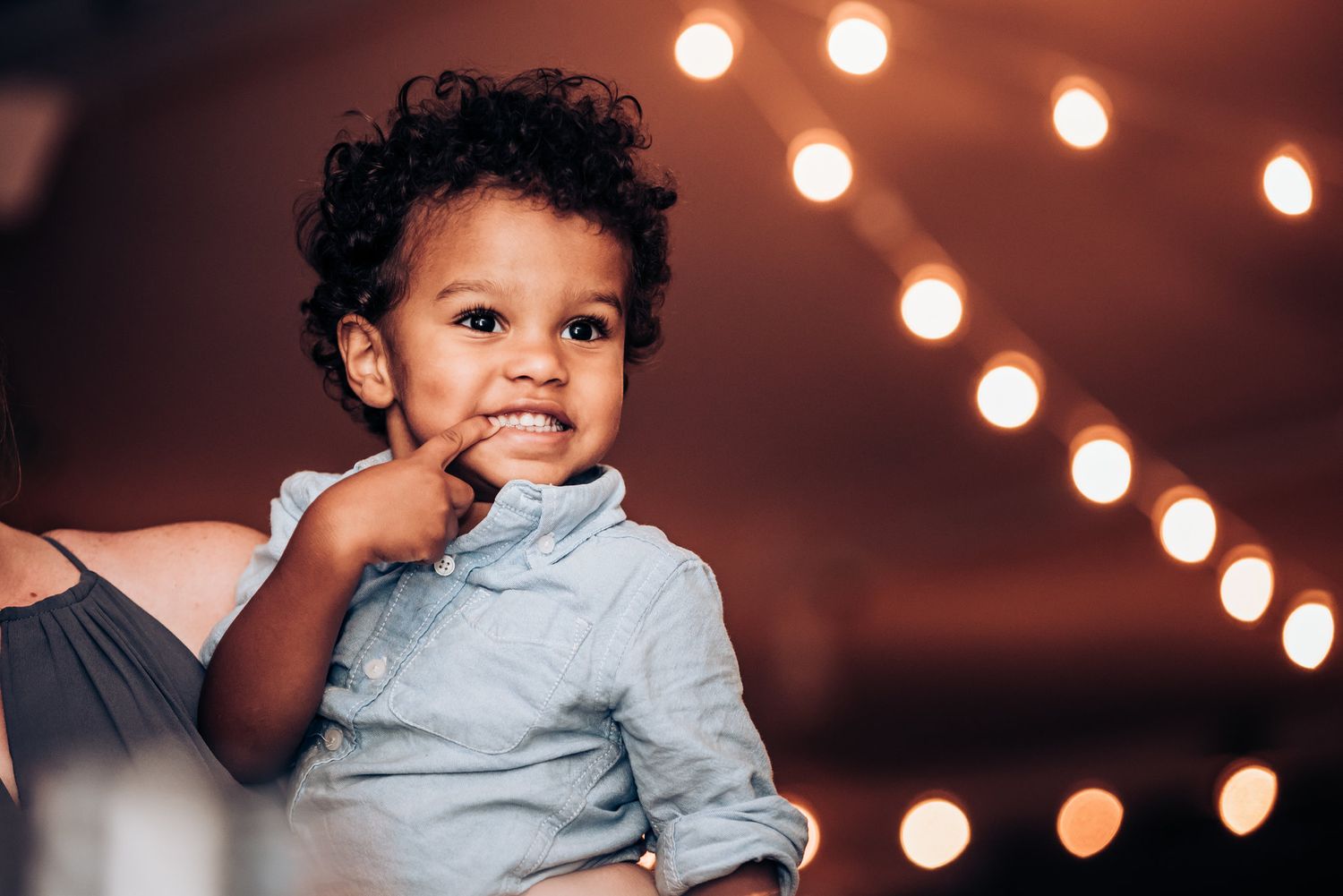 Small child in light blue shirt smiles with joy against a bokeh light background.