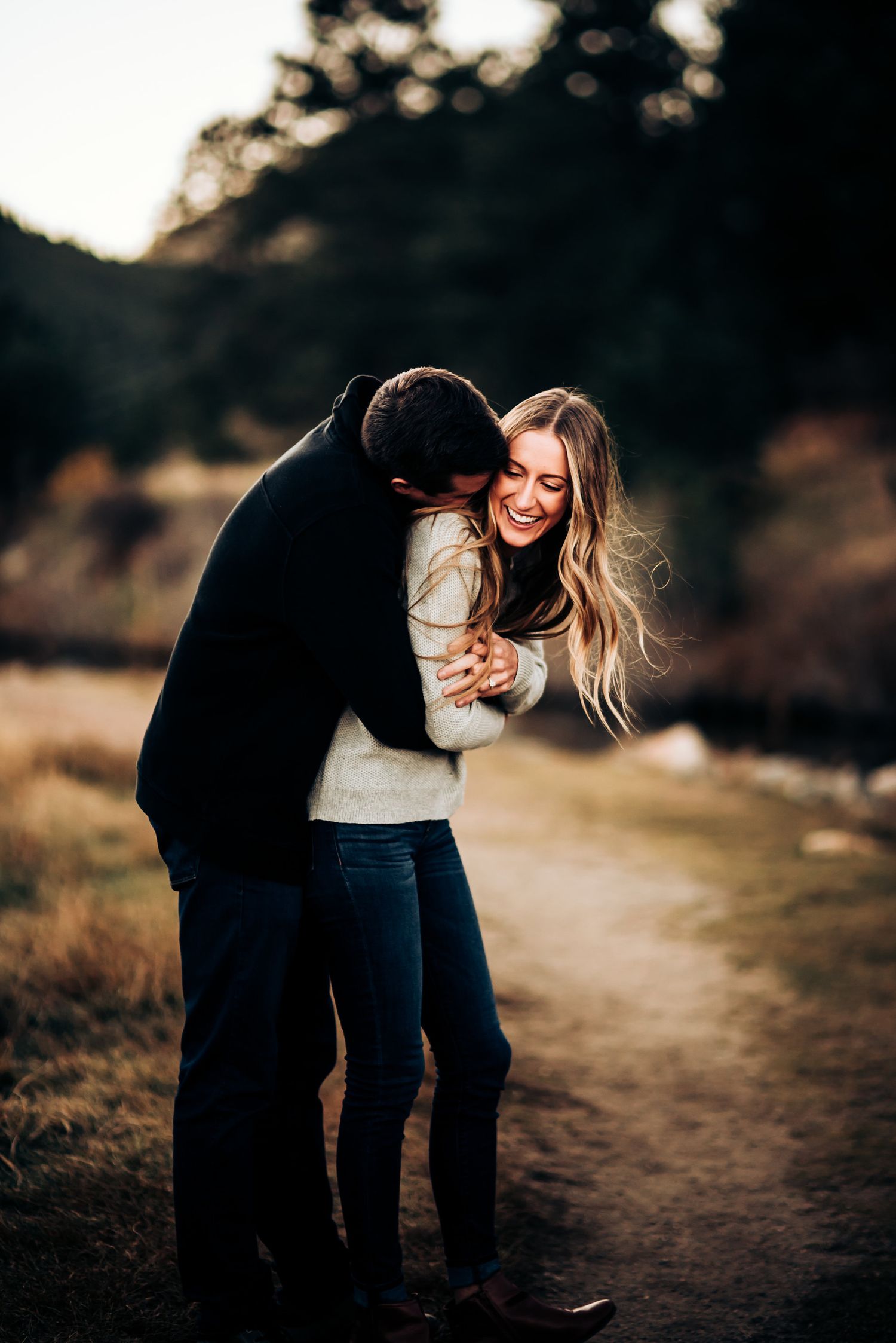 Candid moment of laughter and embrace on autumn trail at sunset.
