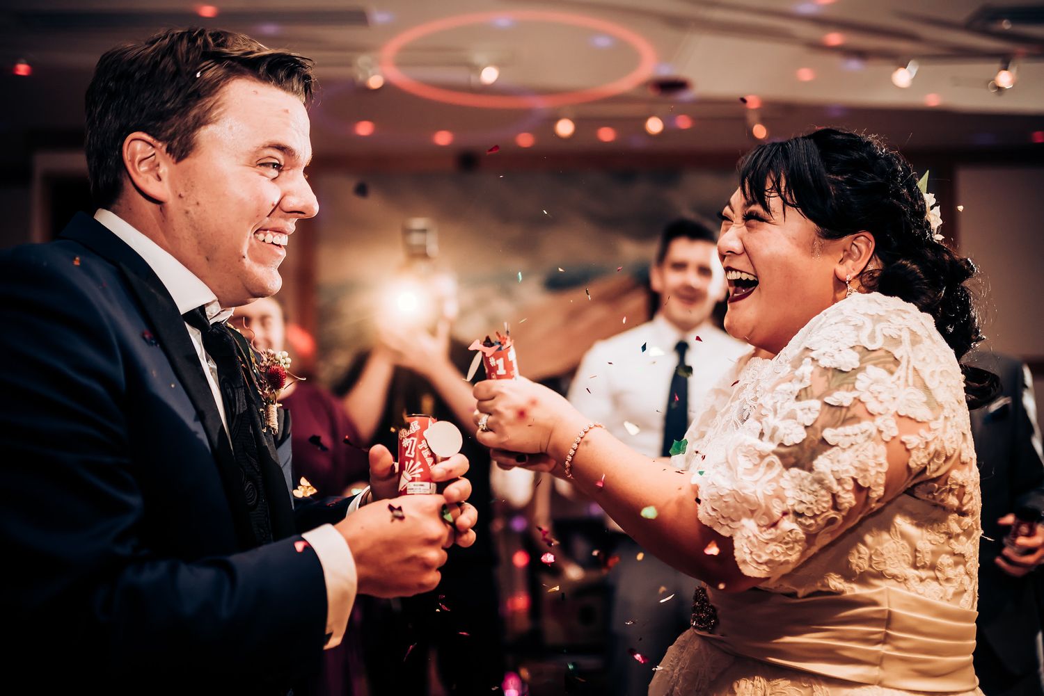 Energetic dancing and laughter at a wedding reception with ambient lighting.