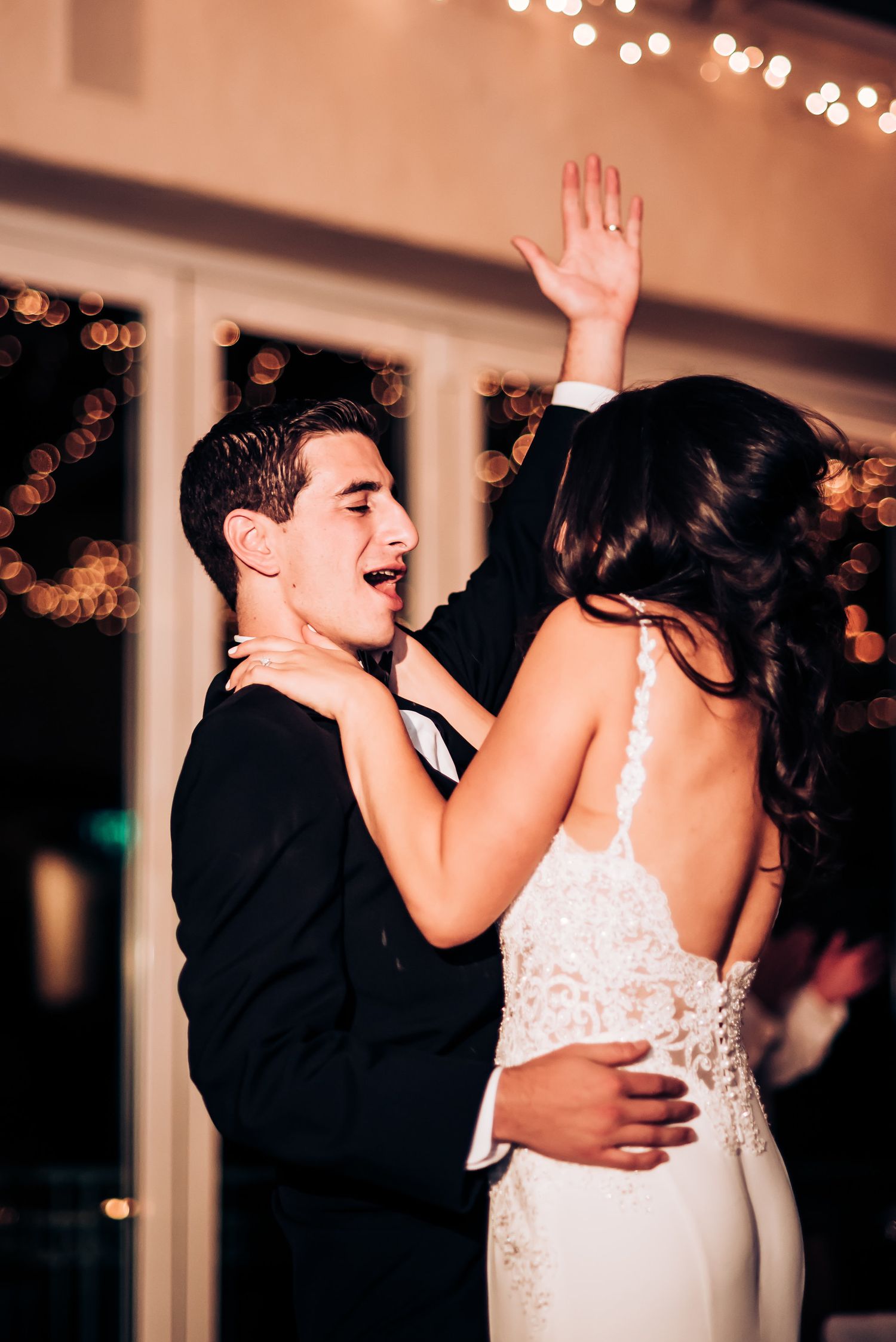 Joyful couple dances energetically during wedding celebration under ambient lighting.