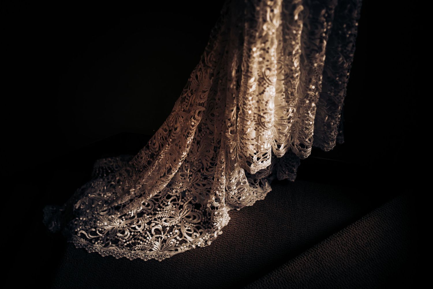An ornate beaded wedding dress train with intricate lace detailing against dark background.