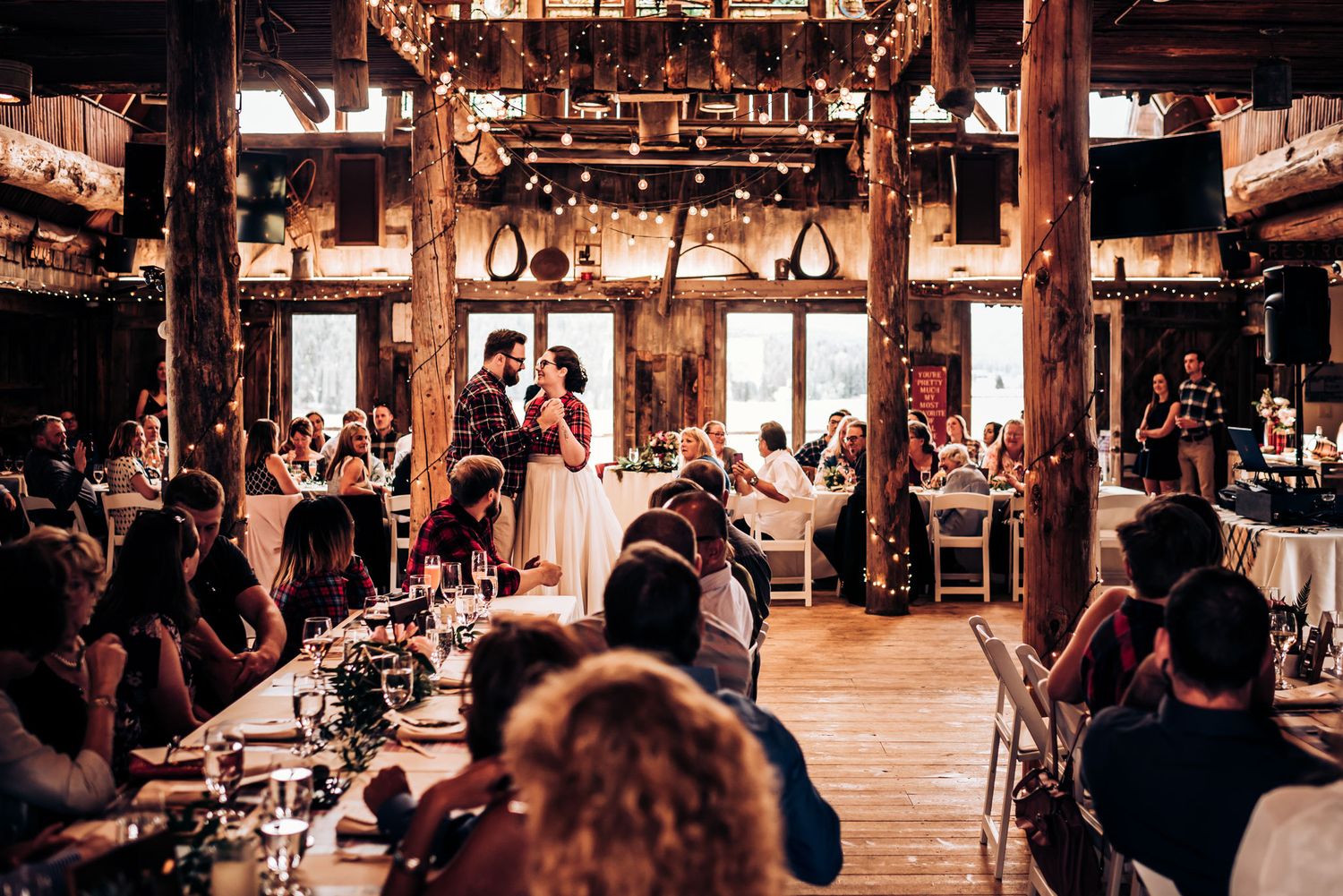Wedding guests gathered in a rustic barn venue with wooden beams and natural lighting.