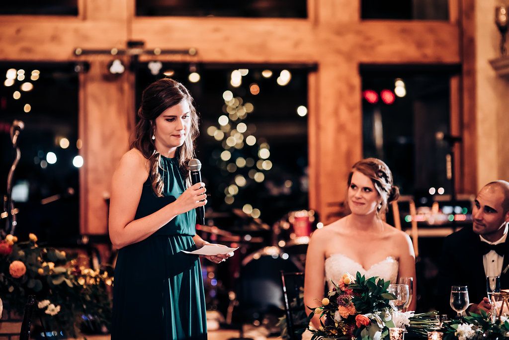 A toast being given during wedding reception with string lights and holiday decor in background.