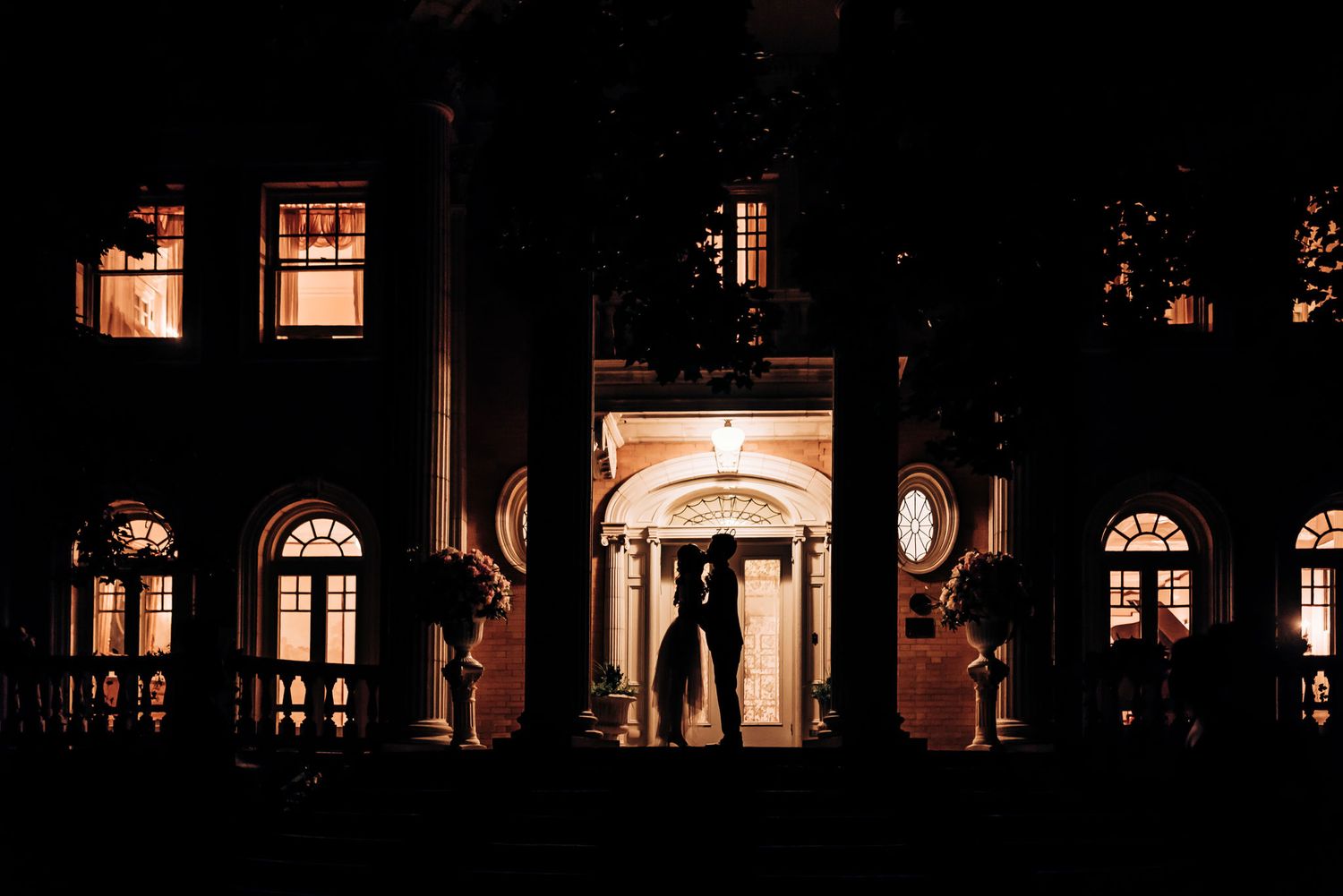 An elegant building lit up at night with a couple's silhouette in the illuminated doorway.