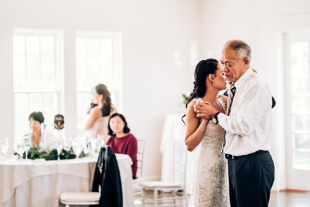 Couple sharing an intimate dance in a bright reception hall with white walls and elegant table settings.