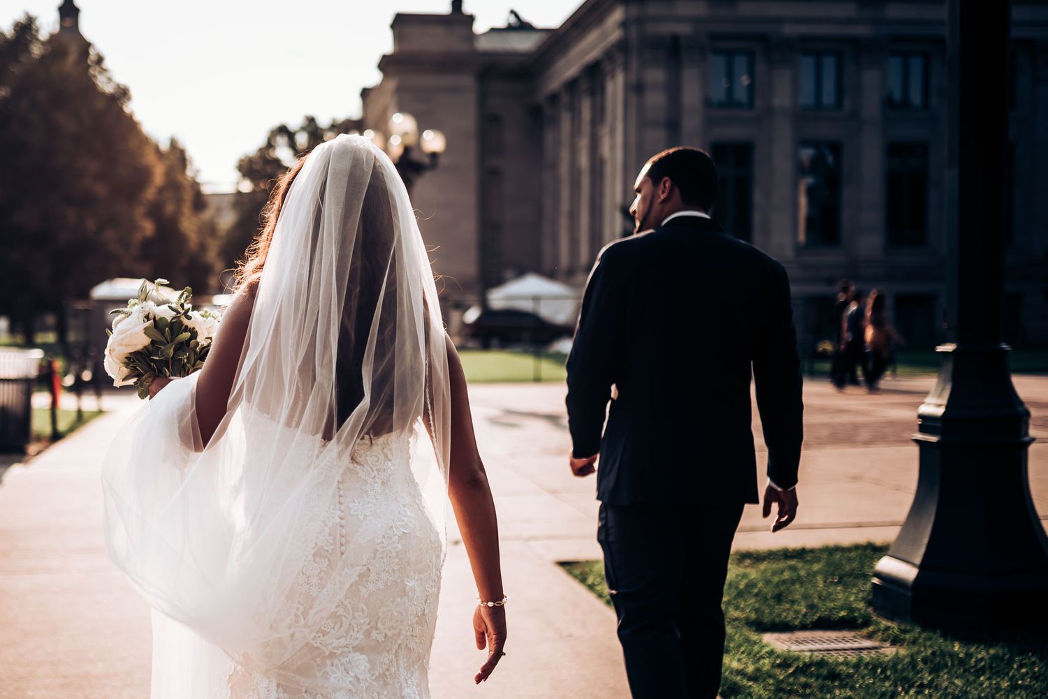 A couple walks away from camera on their wedding day in front of a grand building.