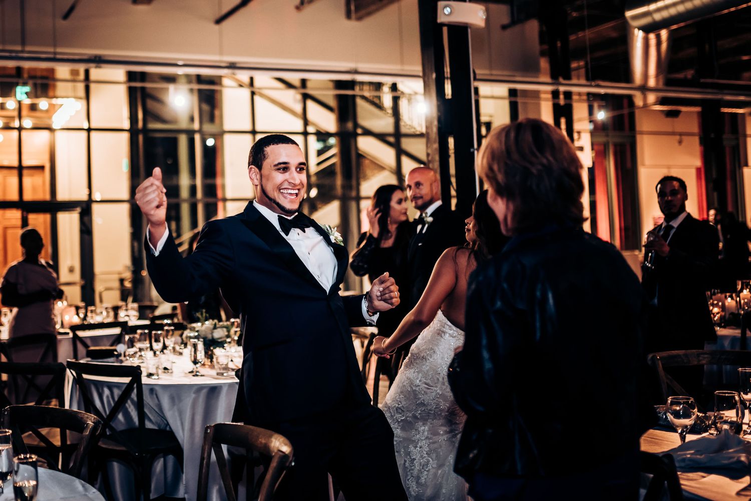 A couple shares a lighthearted moment during their wedding reception with elegant table settings visible.