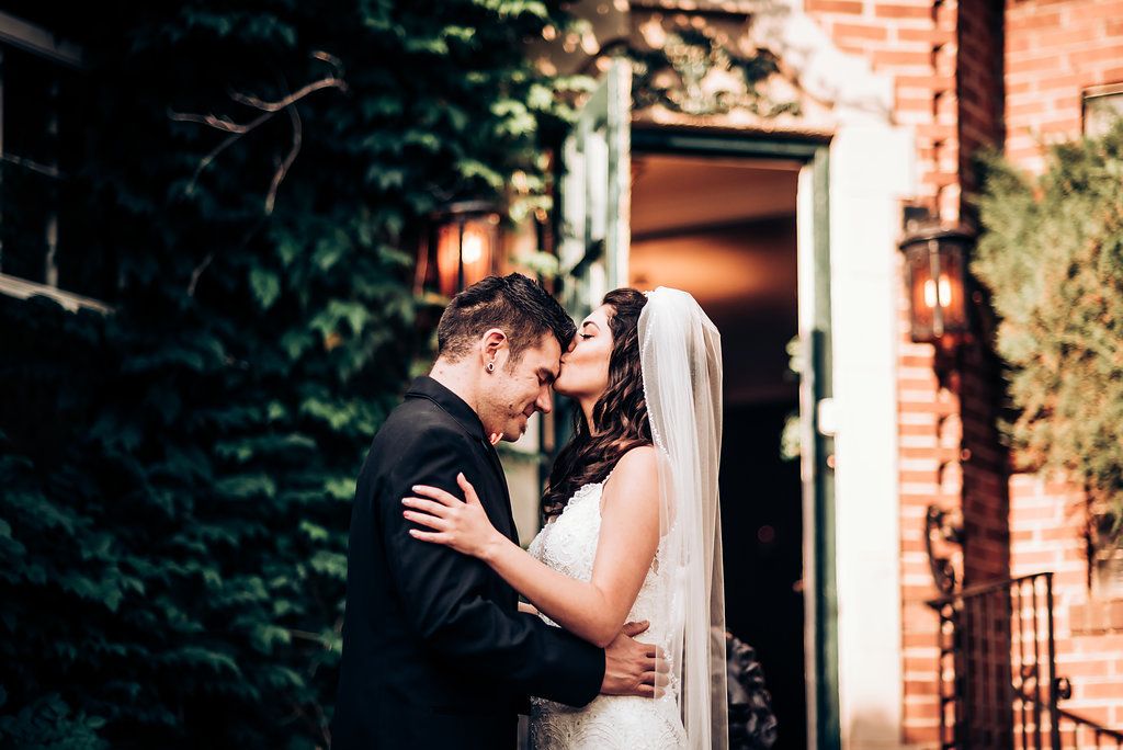 Romantic wedding portrait in front of an ivy-covered brick entrance with warm lighting.