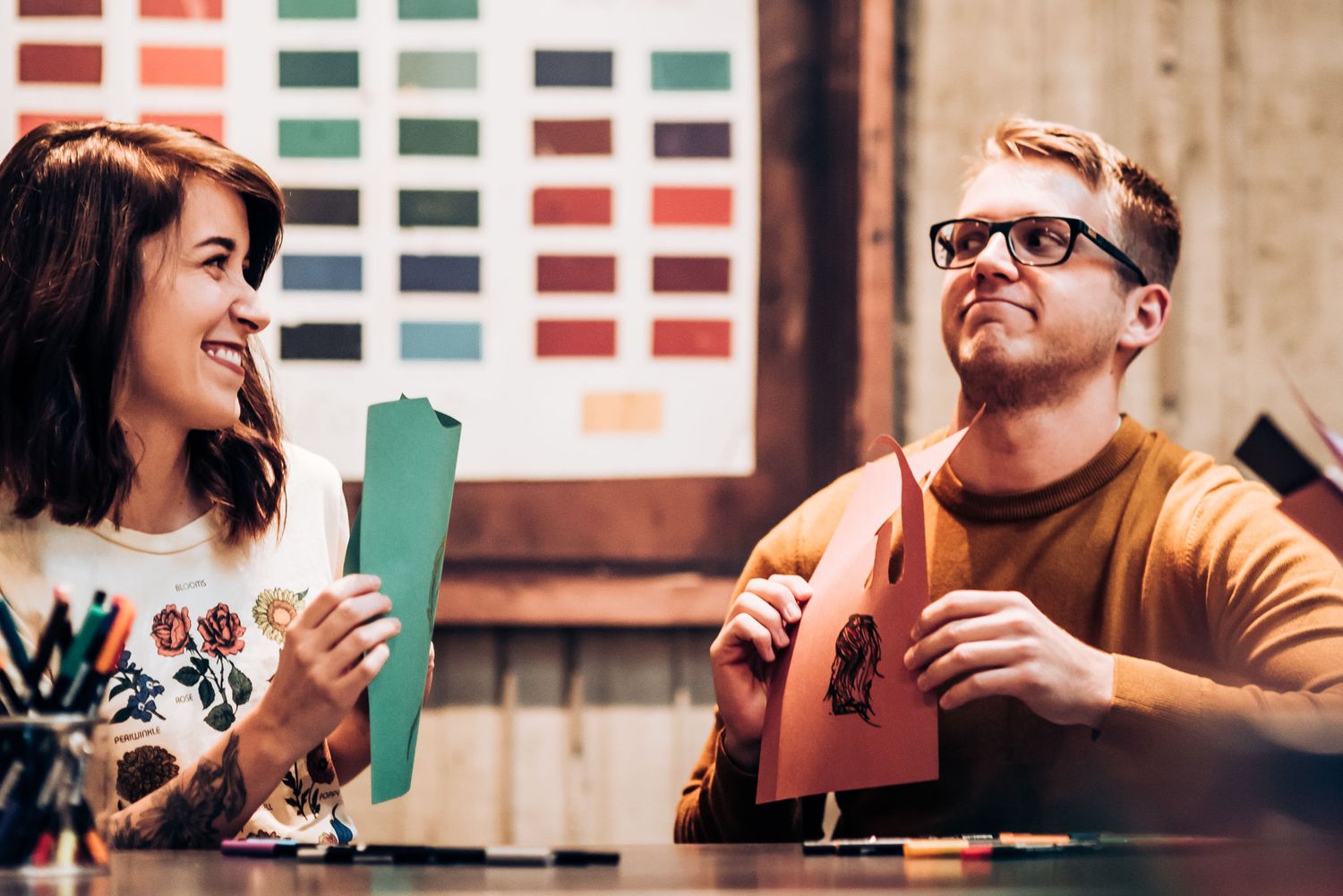 Two people share a lighthearted moment while working on colorful art projects.