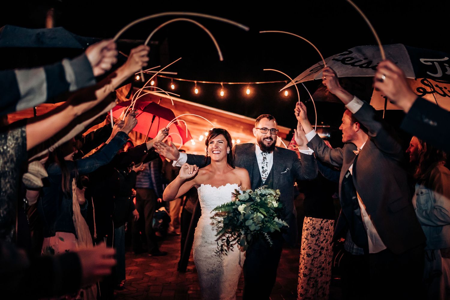 Couple walks through sparkler exit tunnel as wedding guests hold lights overhead.