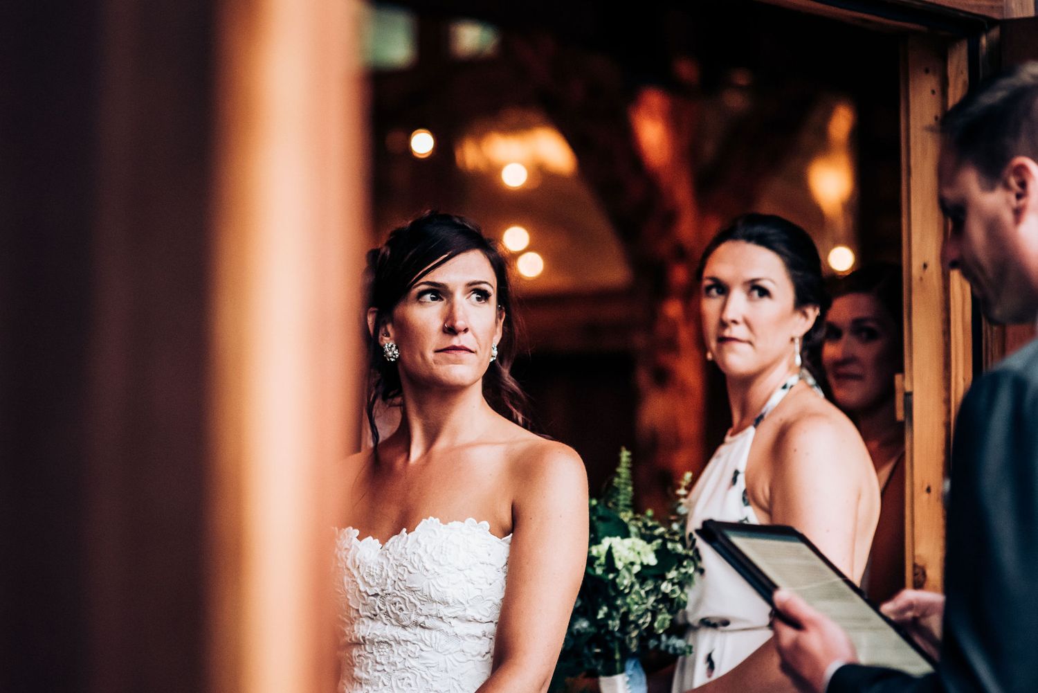 Wedding ceremony in a rustic venue with warm lighting and wooden beams.