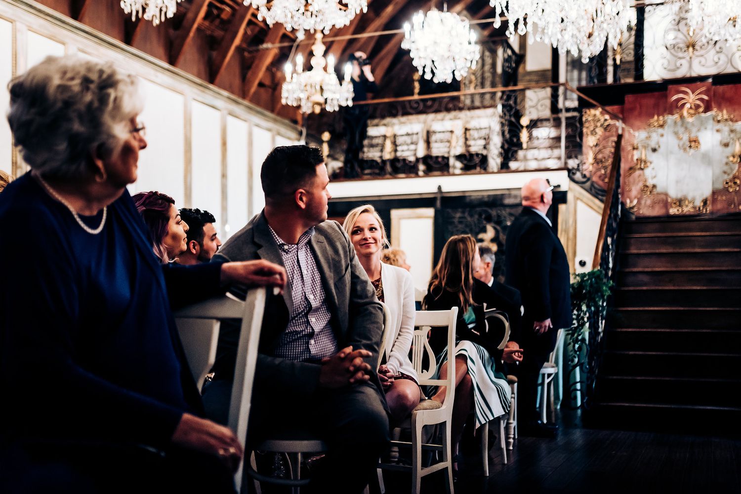 Guests seated beneath ornate crystal chandeliers in a grand historic venue.