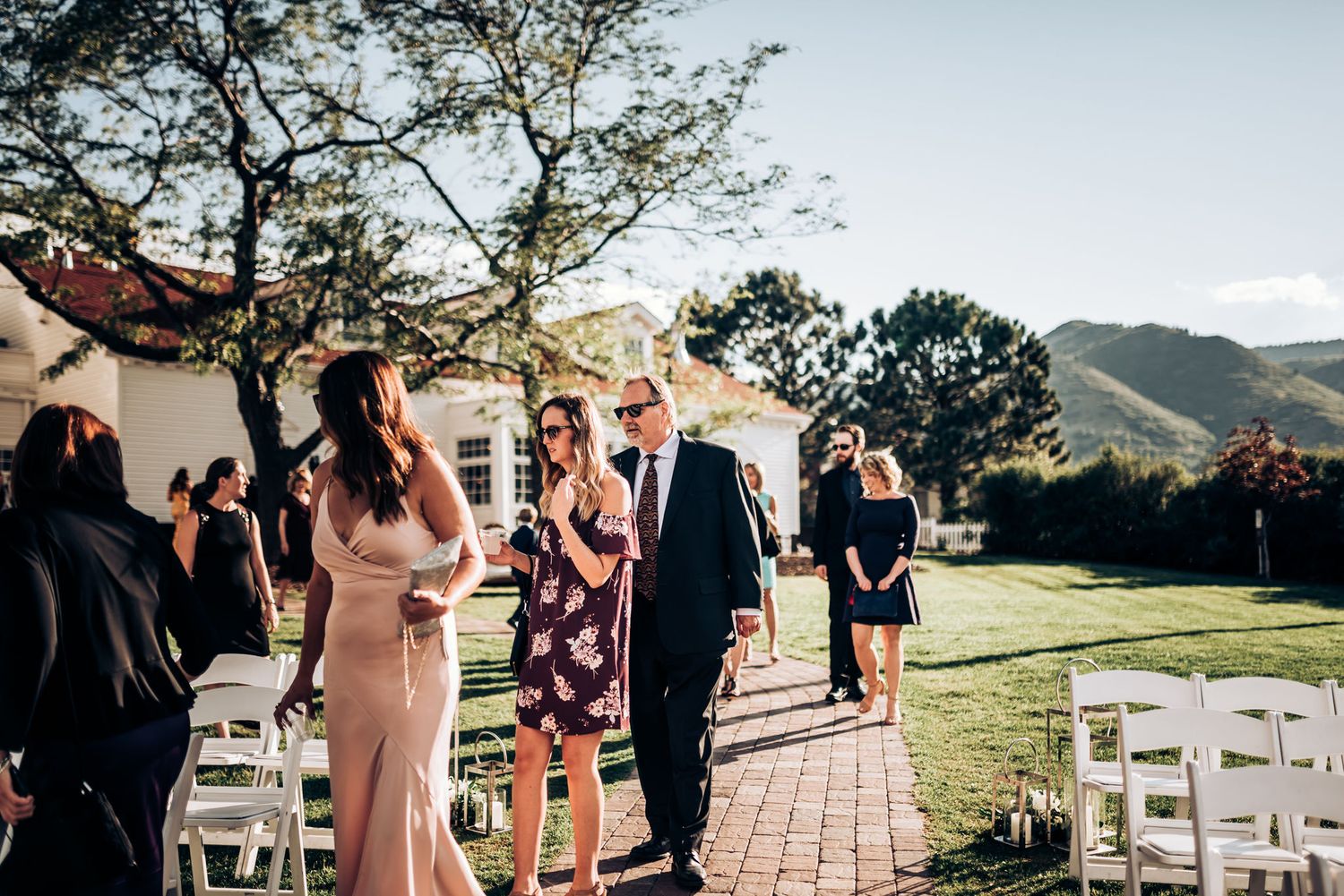 Wedding guests gather for an outdoor ceremony with mountain views and white chairs.