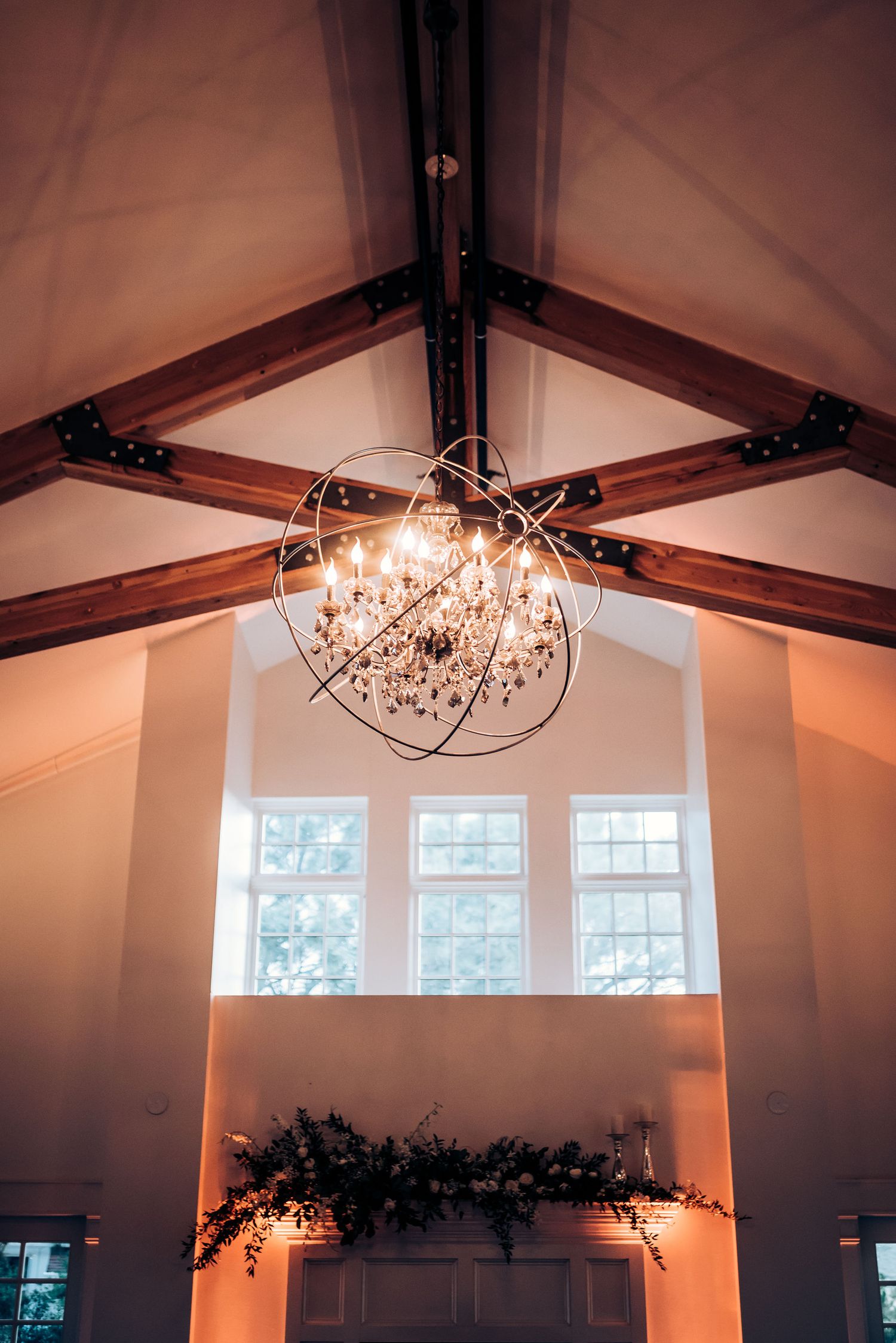 Crystal chandelier hanging from exposed wooden beams in wedding venue.