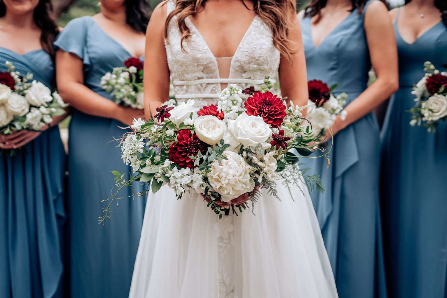 Wedding party showing contrast of white bridal gown against dusty blue bridesmaid dresses with bouquets.