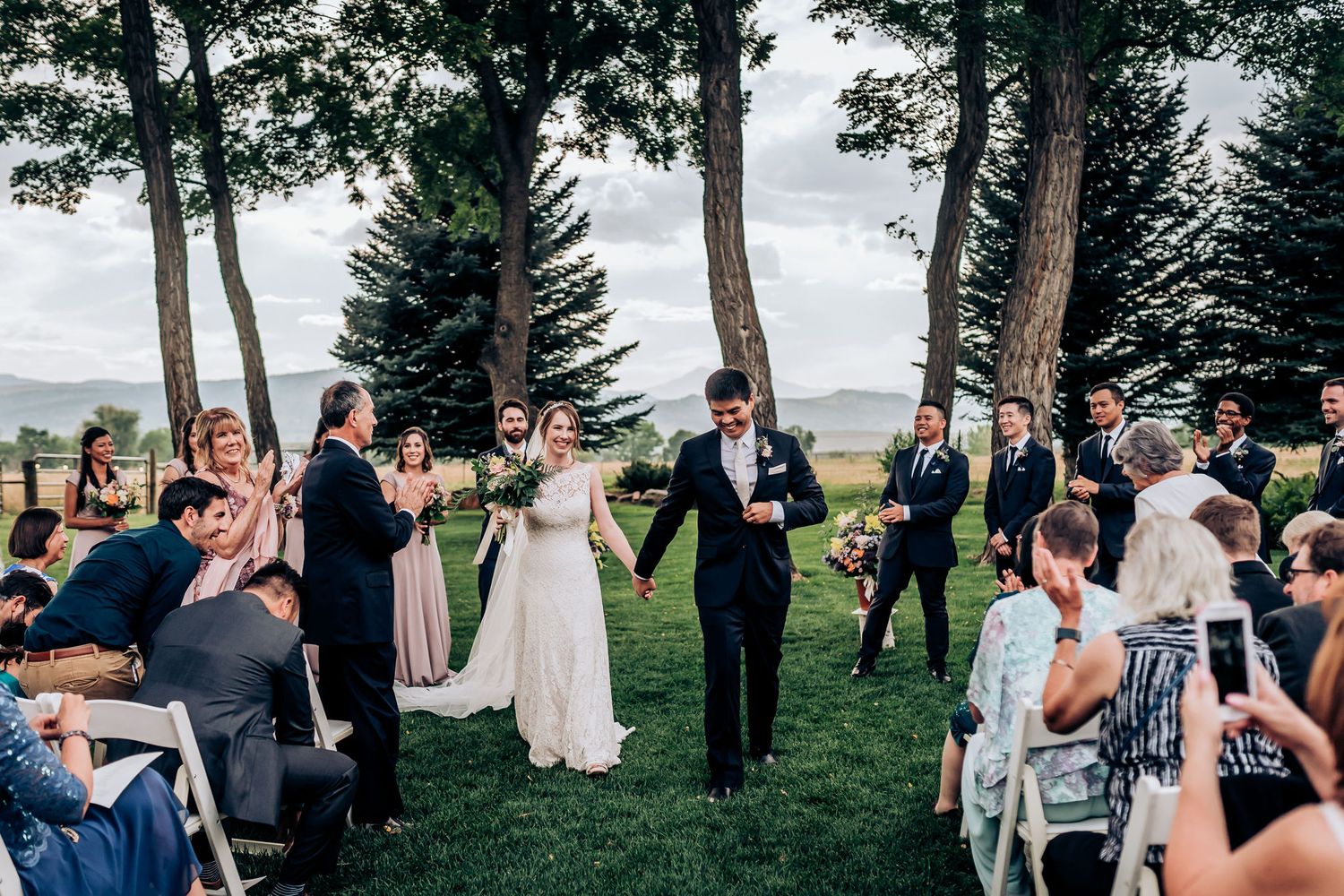 Wedding guests cheer and take photos as the celebration unfolds on a scenic hillside.