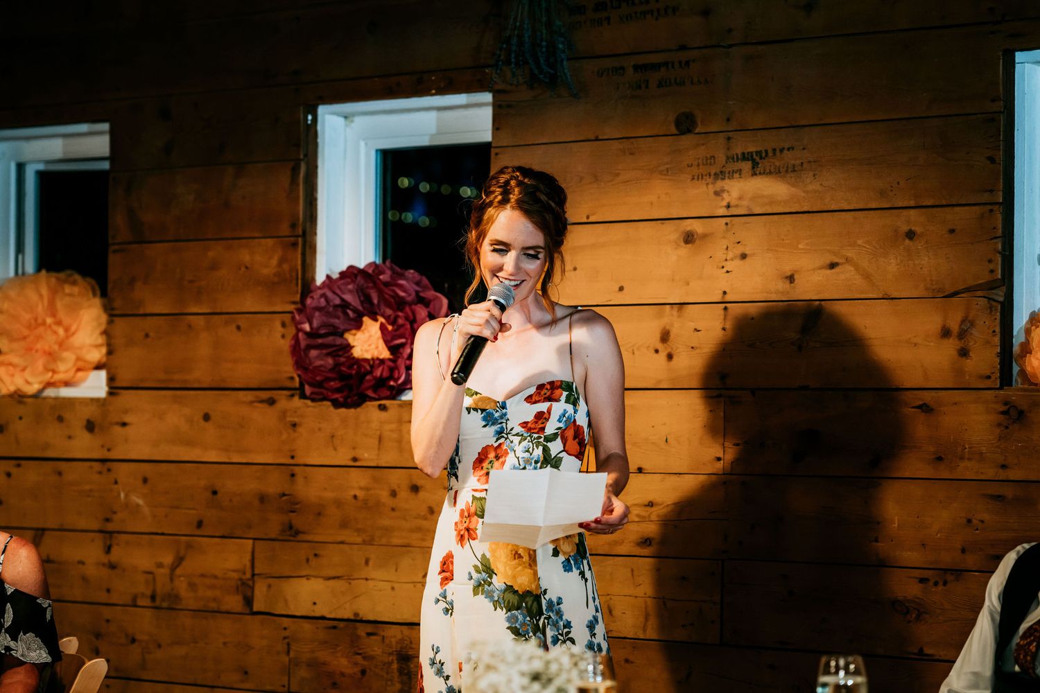 Wedding speech moment in rustic barn venue with wooden wall backdrop and floral decorations.