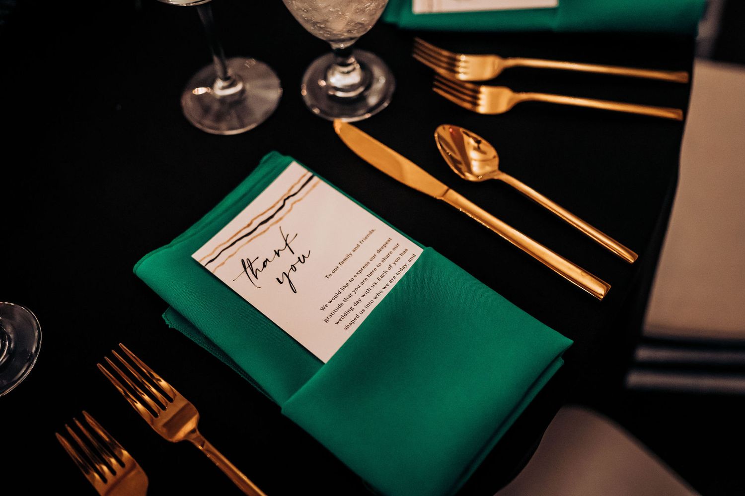 Close-up of formal place setting with emerald napkin and gold utensils.