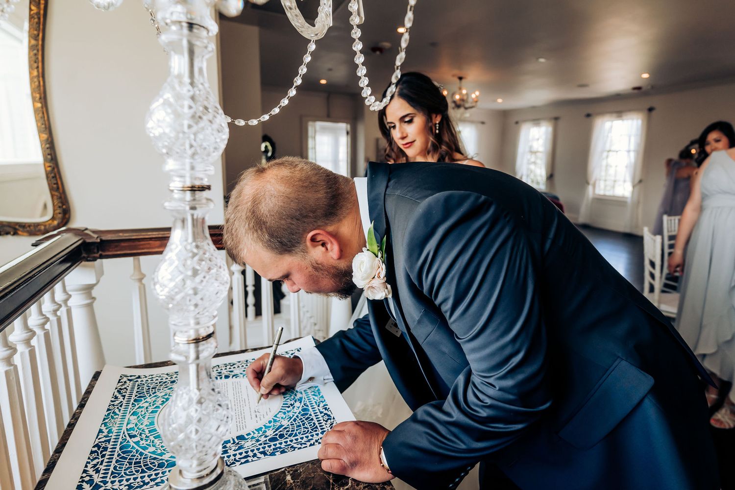 Person signing documents during wedding ceremony under crystal chandelier.