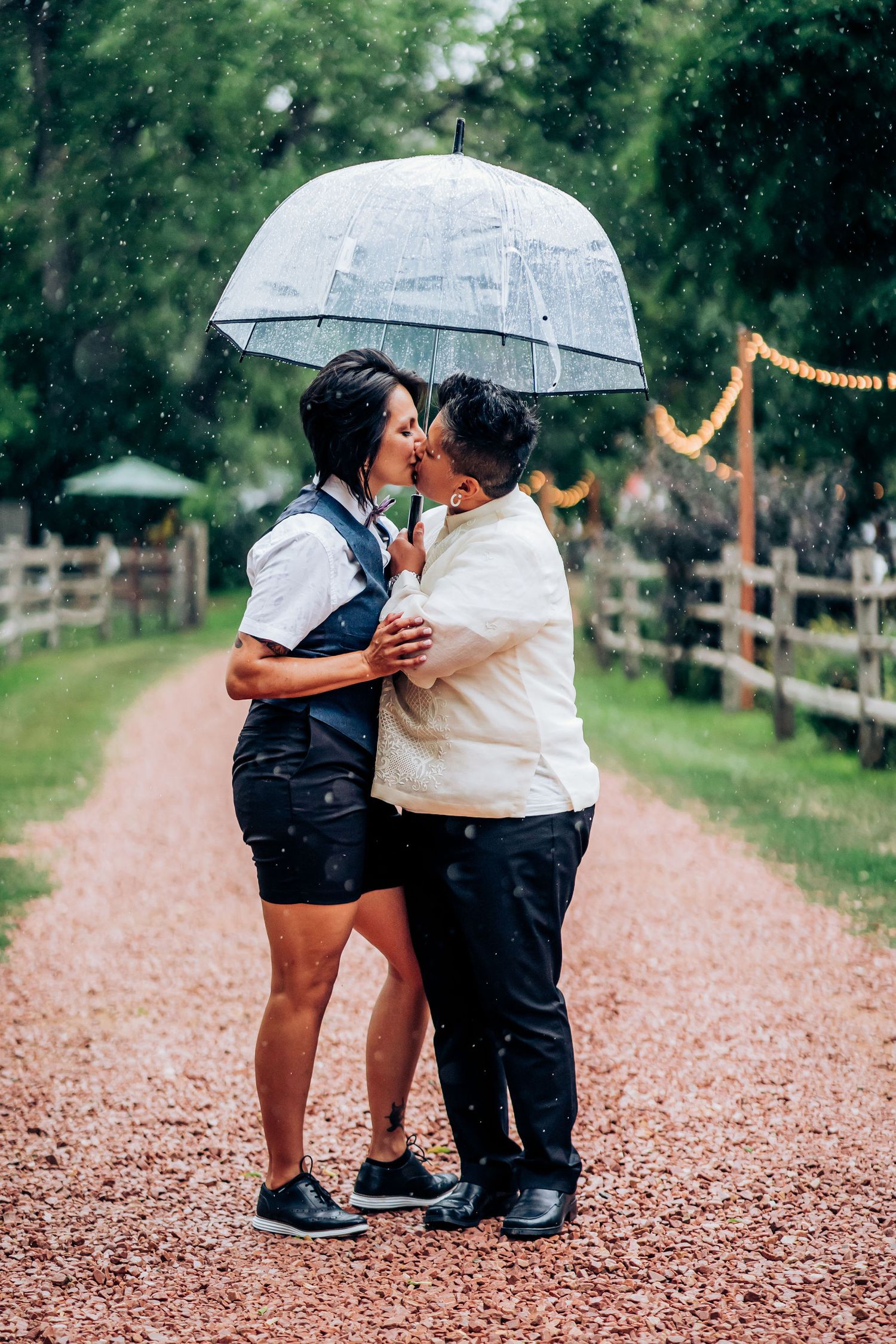 Intimate moment shared under a clear umbrella on a rainy path.