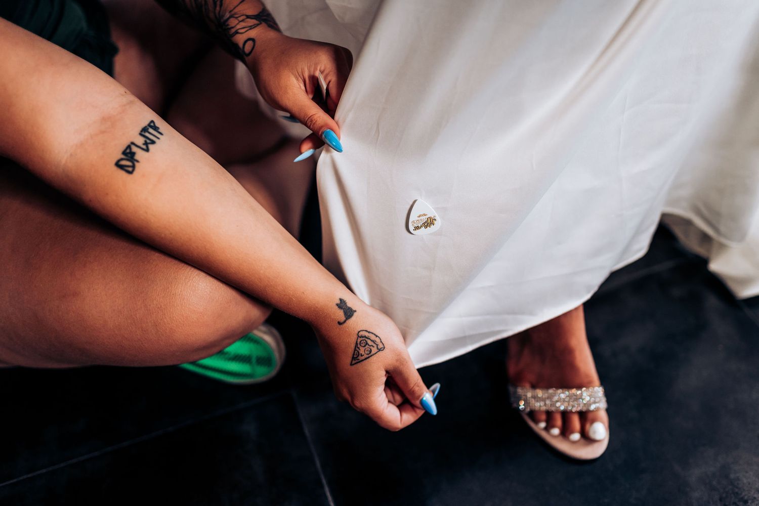 Detail shot of hands adjusting wedding attire with visible tattoo and white sandals.