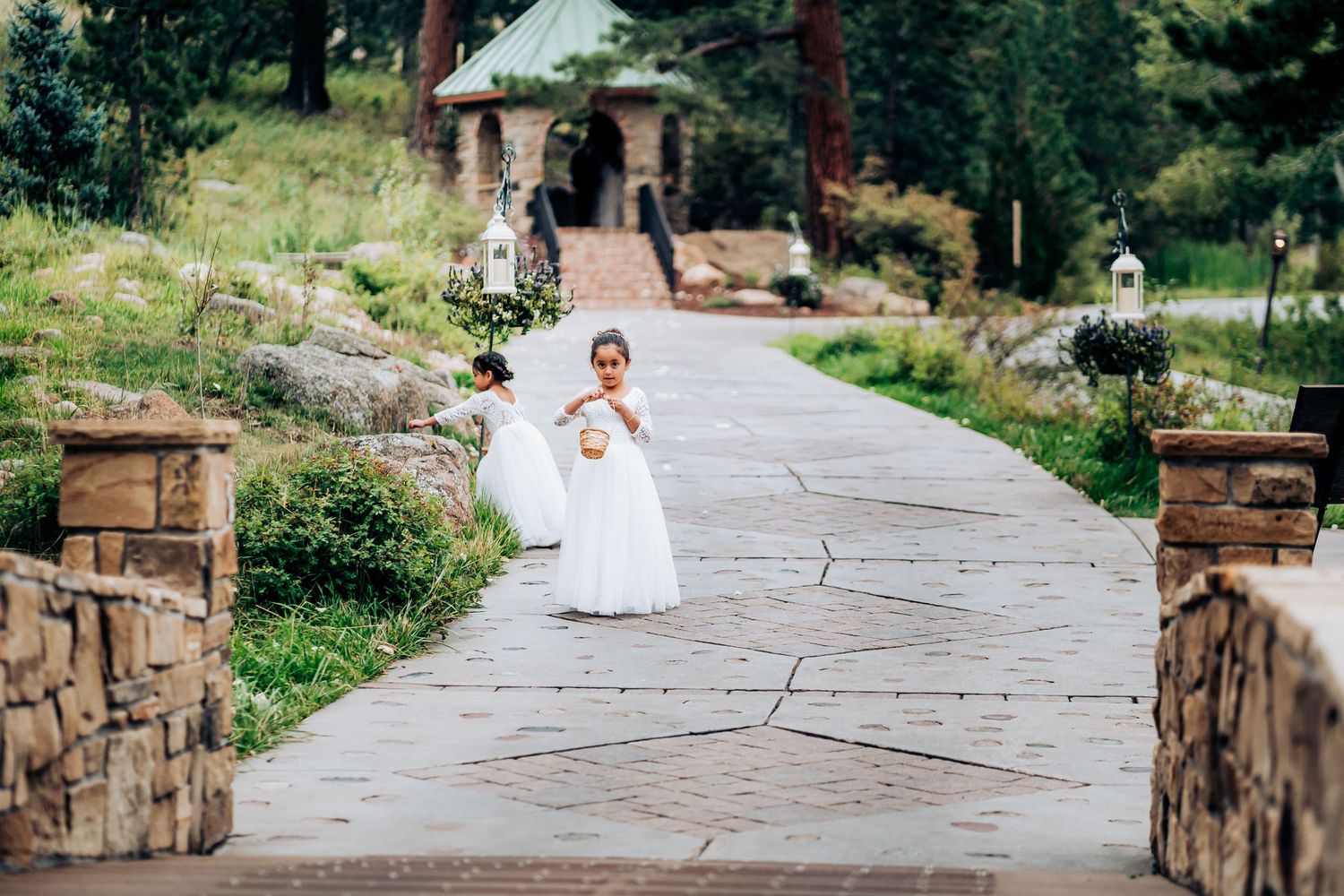 Two attendants in white dresses walk down a stone-lined pathway at an outdoor venue.