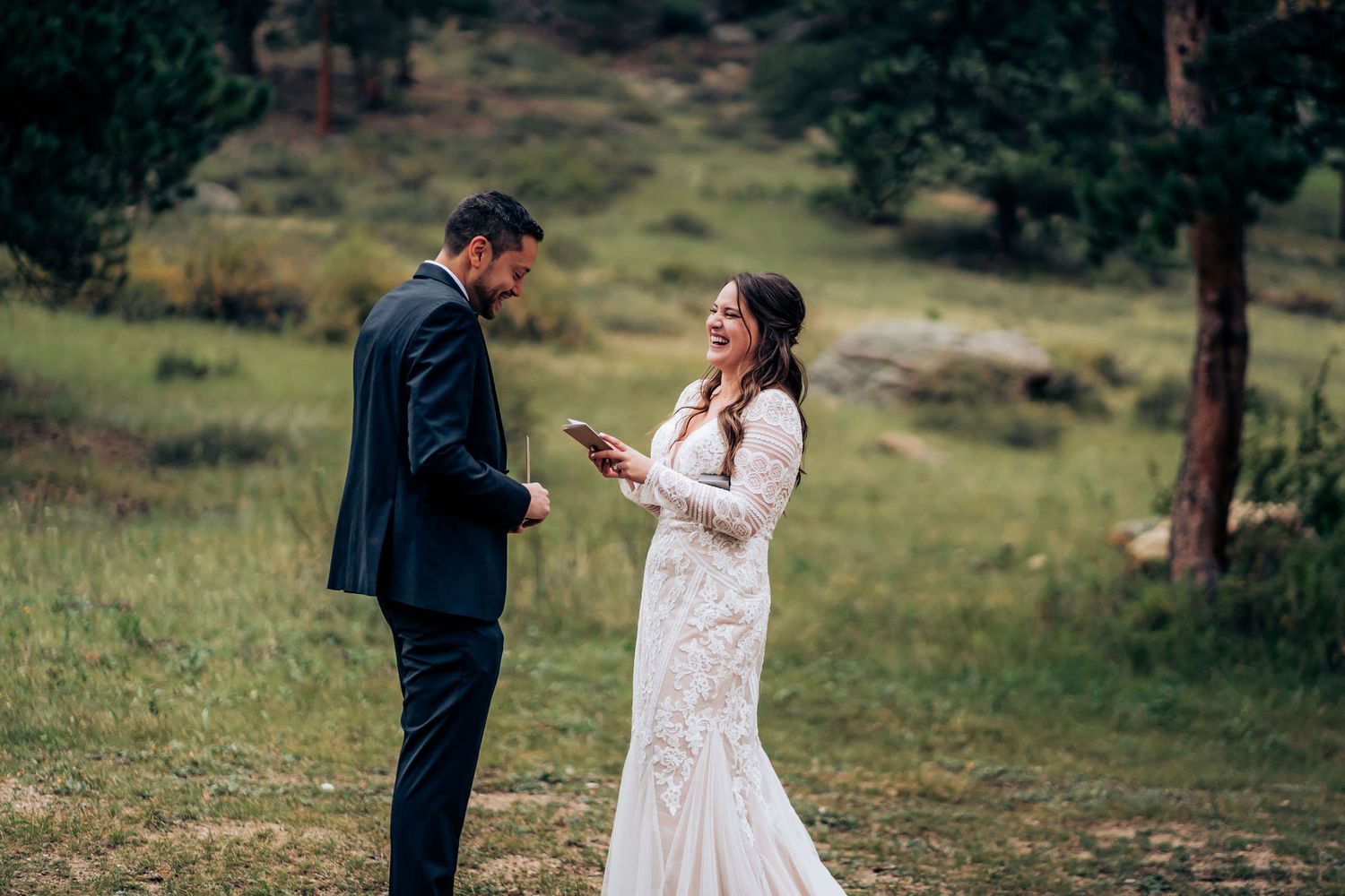 A couple in wedding attire shares intimate moments in a misty mountain meadow surrounded by evergreen trees.