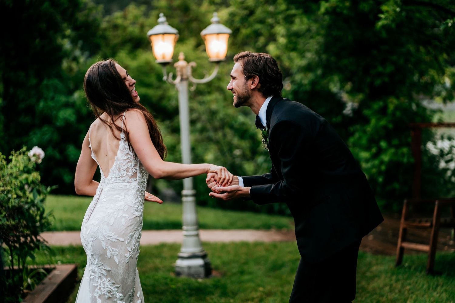 Couple sharing a playful dance moment under vintage lamp posts in a garden setting.