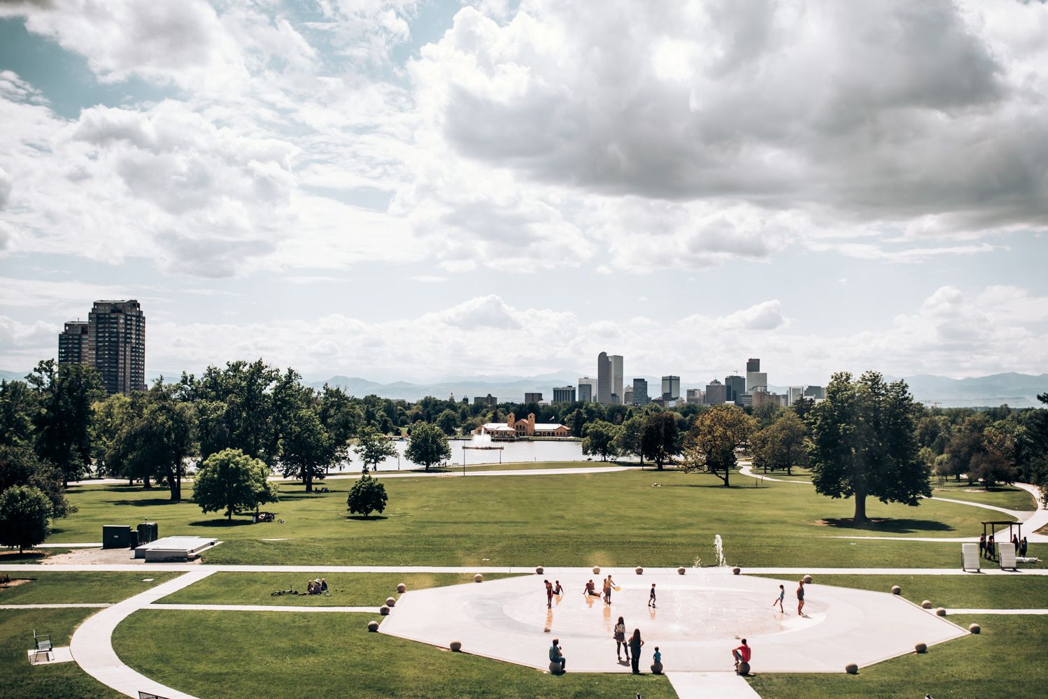Aerial view of a city park with walking paths and buildings in the background under cloudy skies.