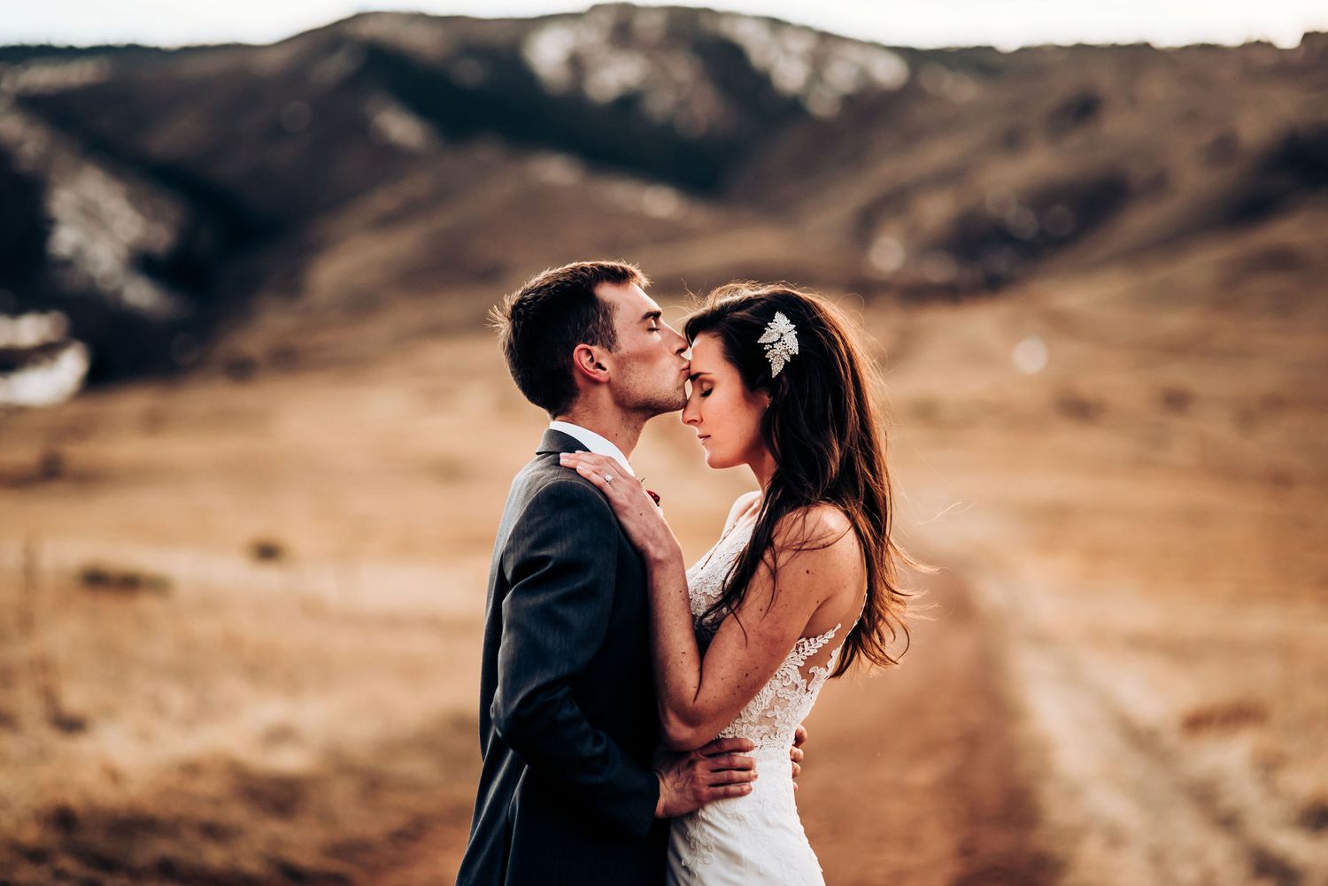 Intimate embrace between couple on mountain trail with golden landscape backdrop.